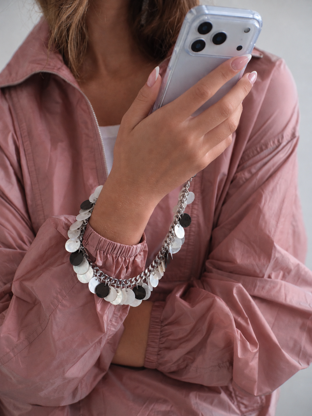 Woman in a pink jacket wearing the Pearl Shells phone chain on her wrist while holding her iPhone
