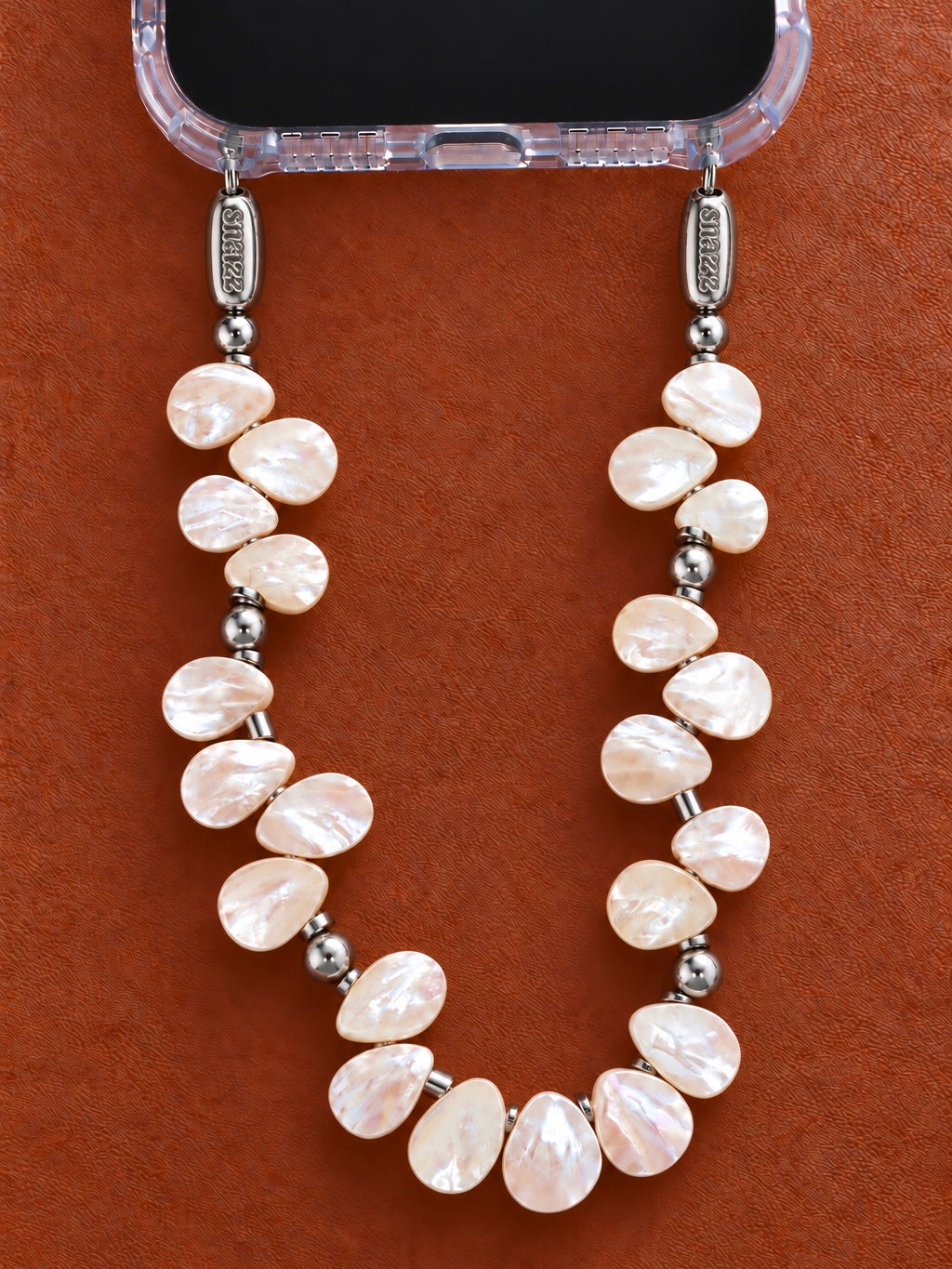 Petal Pearl handmade phone chain hanging from a clear iPhone case on a terracotta background